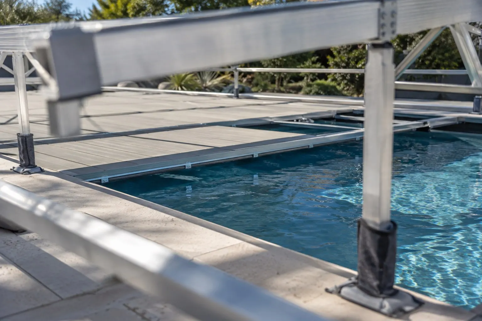 Aluminum support frame being installed over a pool with decking panels partially laid, showing protective padding at the coping